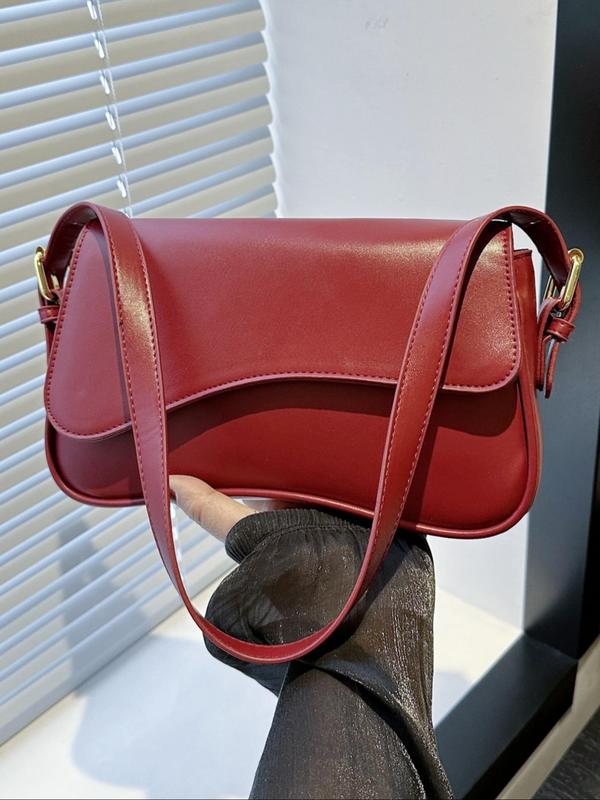 Red leather crossbody bag with gold hardware and front flap, held by gloved hand.