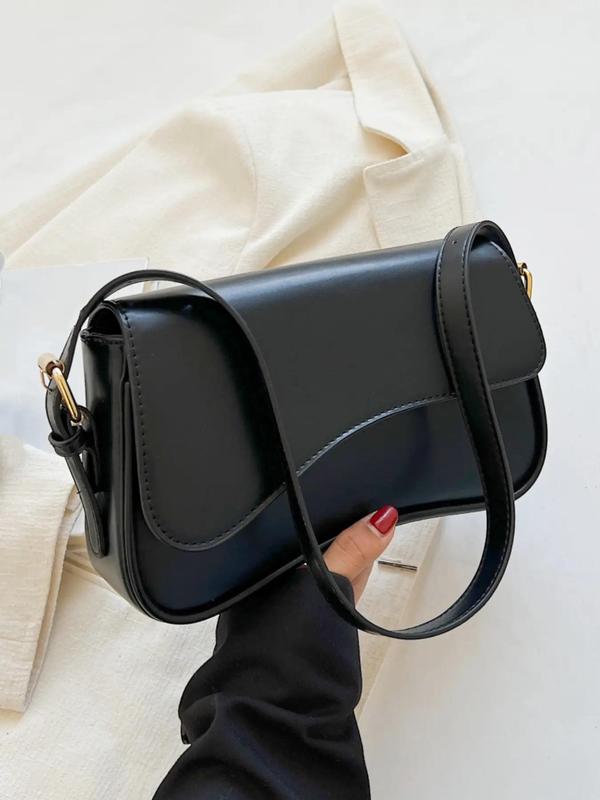 Black leather shoulder bag with front flap and gold hardware held by hand with red nails.