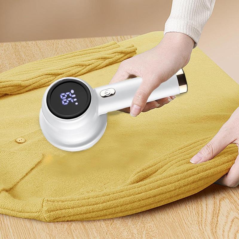 Máquina quitapelusa portátil sobre tejido amarillo, con una mano sujetándola y otra estirando la tela.